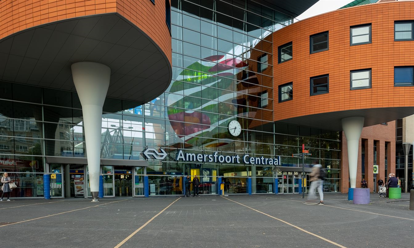  Tekst bij foto voor slechtzienden: Foto van de voorzijde van Amersfoort Centraal station met mensen die in en uitlopen. 